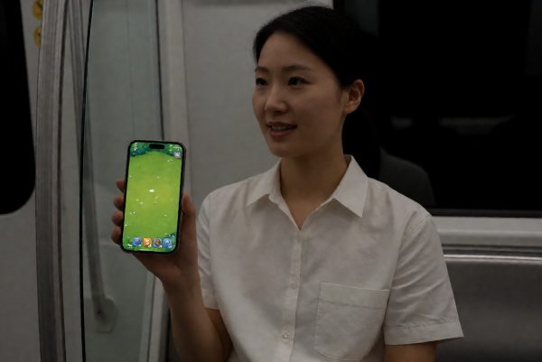 上班族在通勤地铁上单手操作手机,屏幕上显示着塔防类游戏的草坪场景,环境偏暗