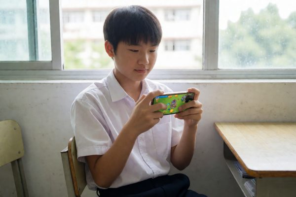 学生在课间用手机横屏玩塔防小游戏,教室窗边自然光线充足,画面轻松日常